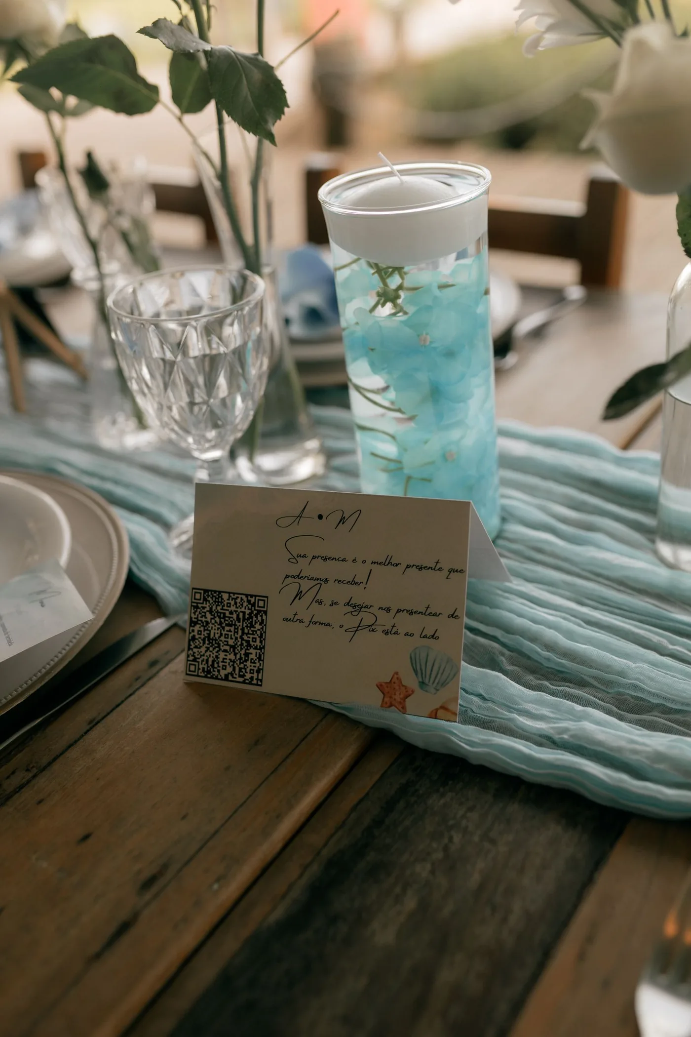 A card with a QR code standing on a set wedding table between a candle and flowers